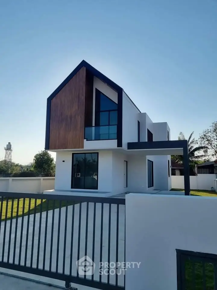 Modern minimalist two-story house with sleek design and large windows, surrounded by a spacious yard and gated entrance.