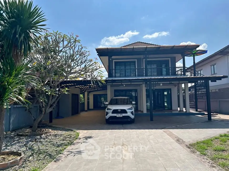 Modern two-story house with spacious driveway and carport, surrounded by lush greenery and clear blue sky.