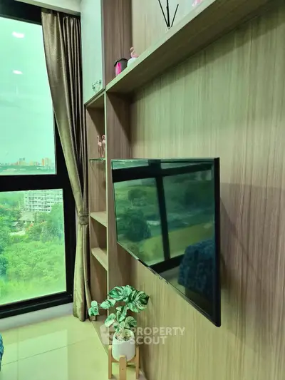 Modern living room with large window and wall-mounted TV, offering a serene green view.