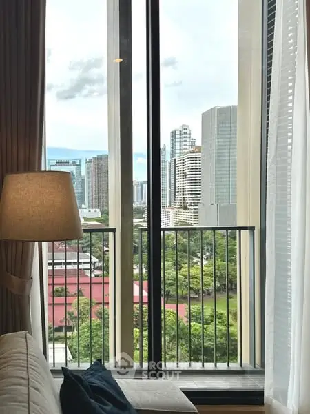 Stunning cityscape view from a modern apartment window with lush greenery and skyscrapers.