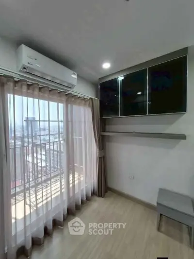 Modern living room with large window and air conditioning, featuring sleek storage cabinets and light wood flooring.