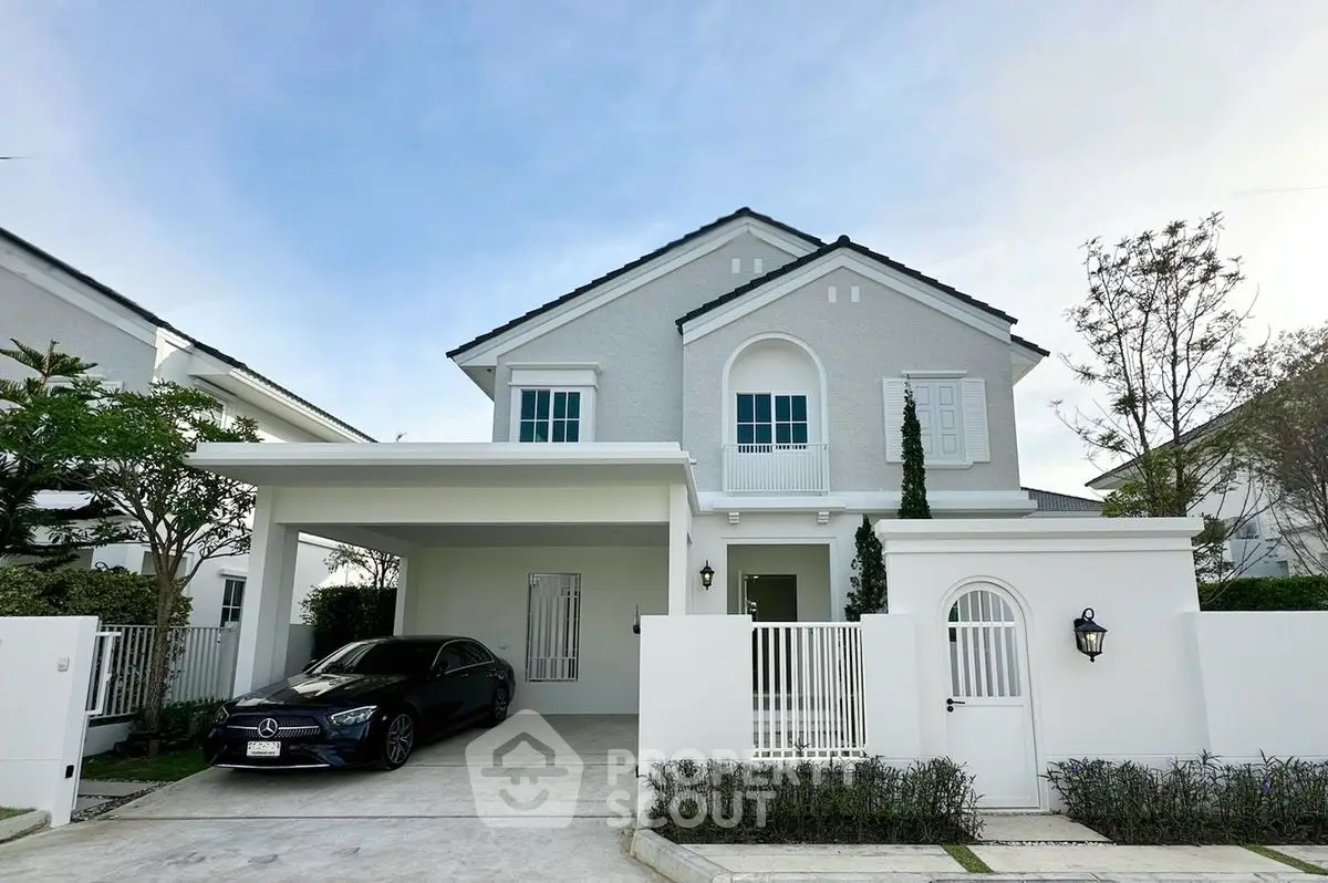 Elegant two-story white house with carport and luxury car in driveway, surrounded by lush greenery.