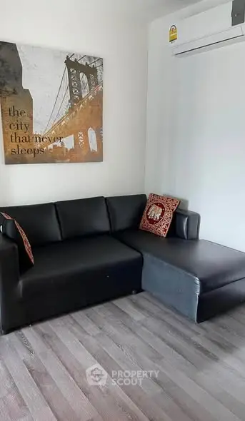 Modern living room with black leather sofa and stylish wall art, featuring sleek flooring and air conditioning.