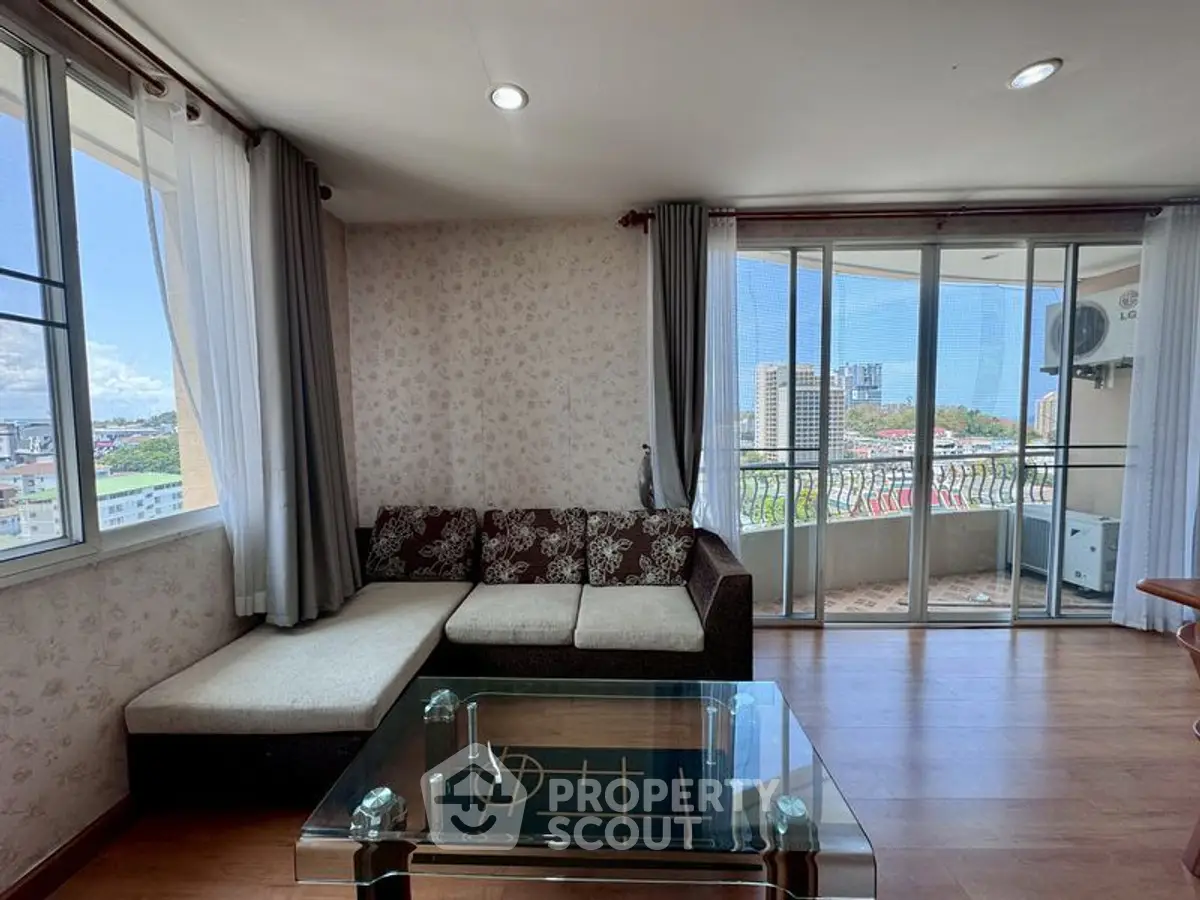 Spacious living room with large windows and balcony offering stunning city views.