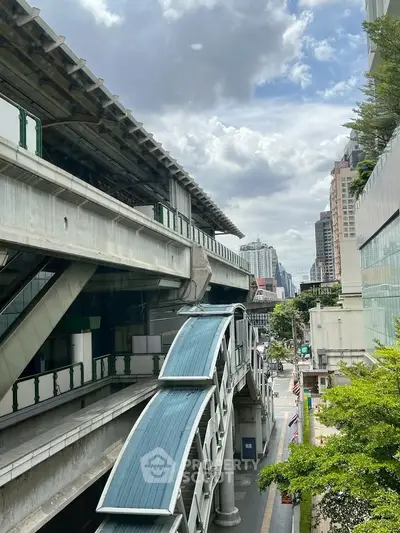 Urban cityscape with elevated train tracks and modern buildings under a cloudy sky.