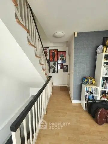 Stylish modern hallway with wooden flooring and staircase, featuring wall art and a bookshelf.