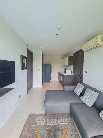 Modern living room with sleek kitchen, cozy gray sofa, and wall-mounted TV in open layout apartment.
