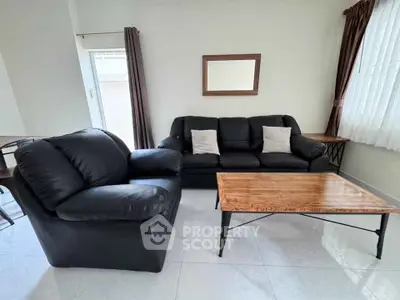 Spacious living room with modern black leather sofas and elegant wooden coffee table.