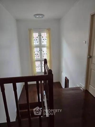 Charming staircase with wooden railing and natural light from window, perfect for cozy home ambiance.