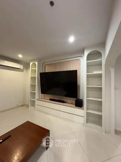 Modern living room with built-in shelves and large TV, featuring sleek design and ambient lighting.