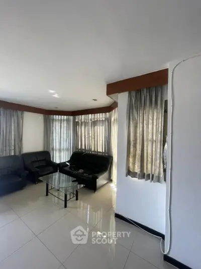Spacious living room with modern black leather sofas and large windows for natural light.