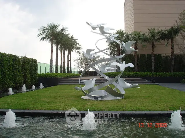Modern sculpture in landscaped garden with water features and palm trees, enhancing luxury real estate appeal.