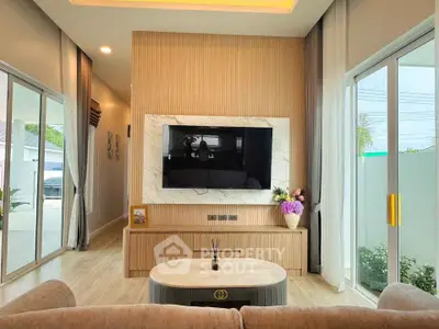 Modern living room with large TV, elegant decor, and sliding glass doors leading to outdoor space.