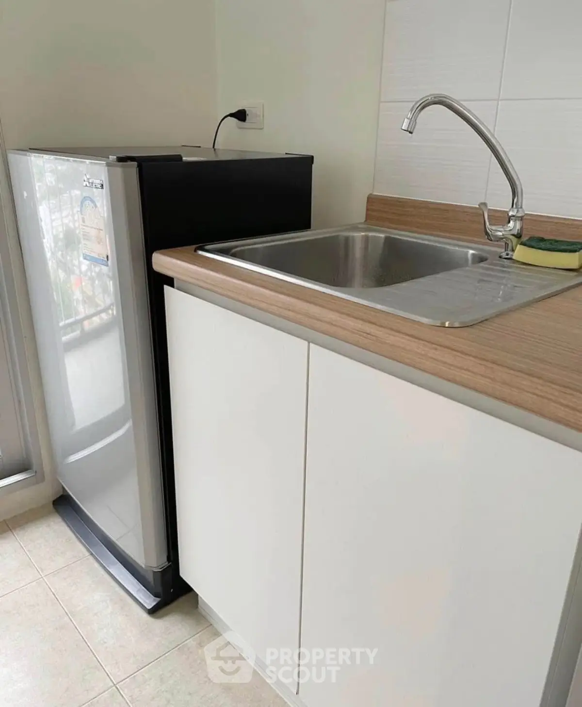 Modern kitchen with sleek fridge and stainless steel sink in compact layout.