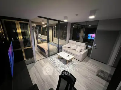 Modern open-plan living room with glass-walled bedroom, stylish decor, and cozy seating area.