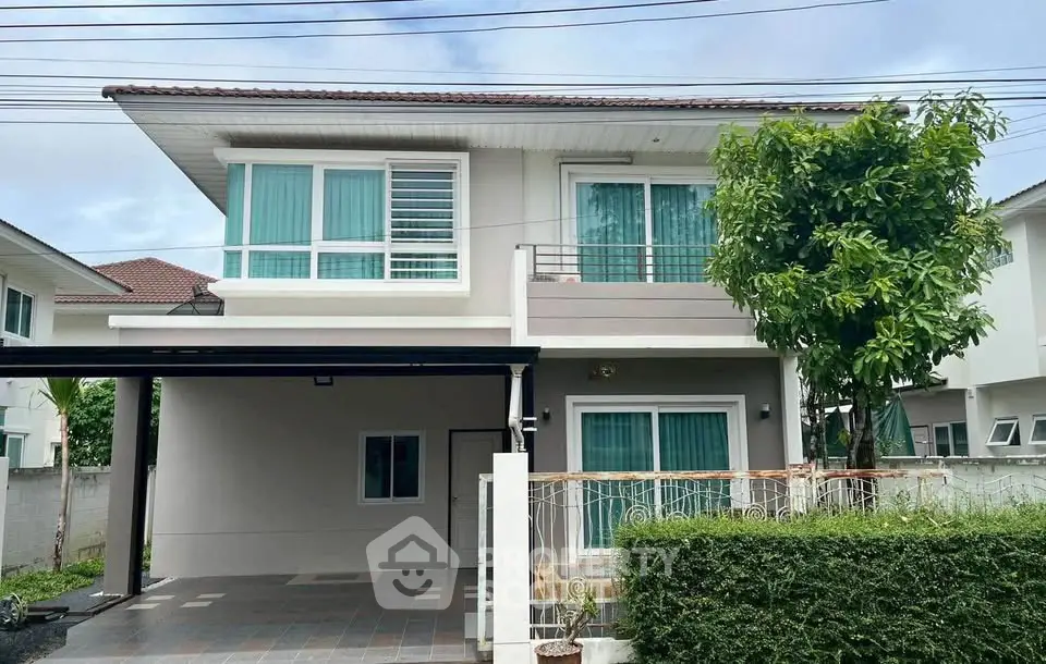 Modern two-story house with balcony and carport in a suburban setting.