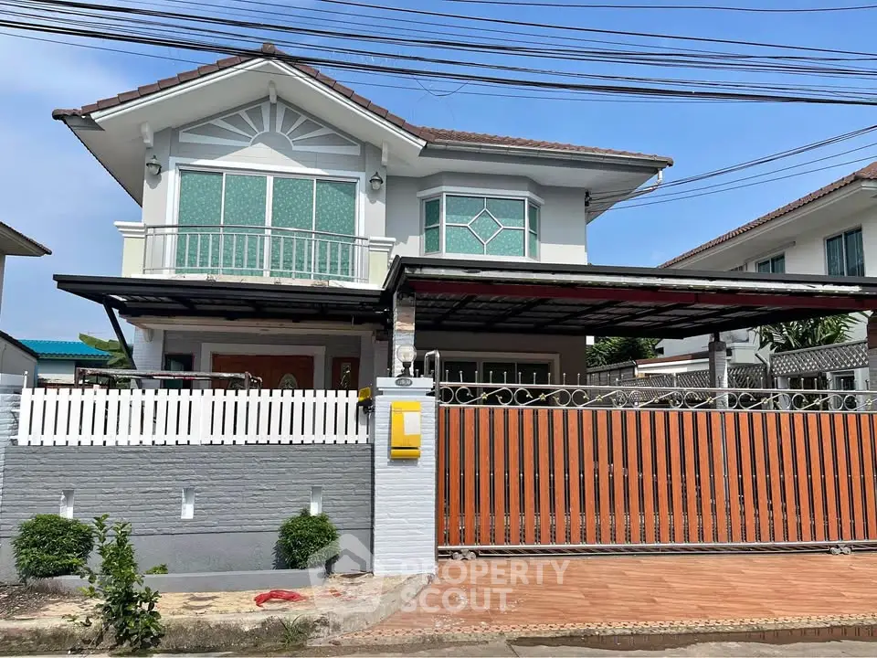 Charming two-story house with balcony and gated entrance in a serene neighborhood.