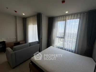 Modern bedroom with large windows and city view, featuring a comfortable bed and stylish sofa.