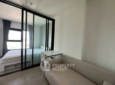 Modern studio apartment with glass partition, cozy sofa, and natural light.