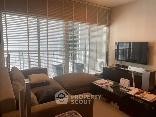 Modern living room with large sofa and wall-mounted TV, featuring floor-to-ceiling windows and blinds.