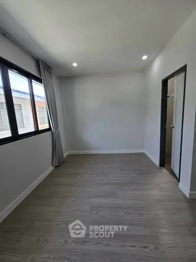 Spacious unfurnished room with large window and modern flooring, perfect for customization.