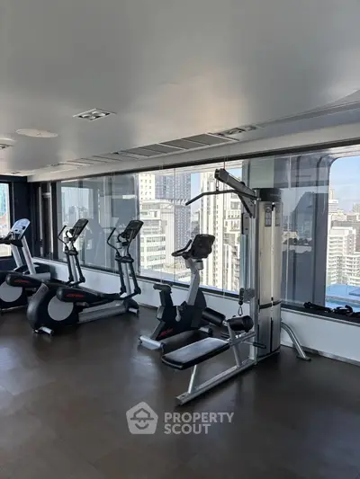 Modern gym with city view featuring exercise equipment and large windows.
