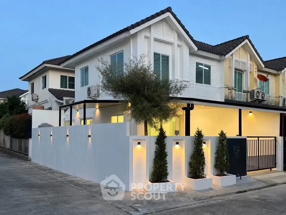 Charming two-story white house with modern exterior lighting and landscaped front yard in a serene neighborhood.