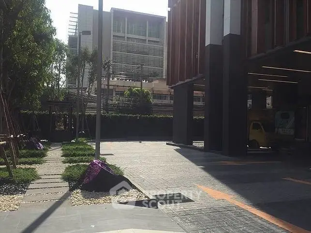 Modern building entrance with landscaped walkway and urban surroundings.