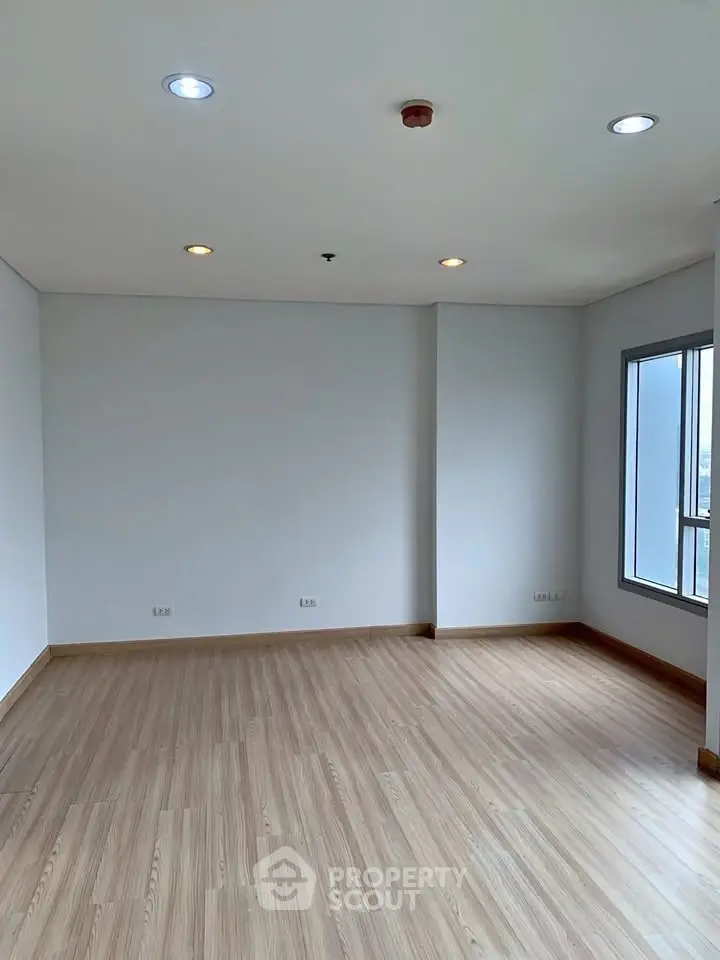 Spacious empty room with wooden flooring and large window, perfect for customization.