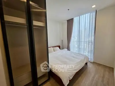 Modern bedroom with large window and city view, featuring sleek wardrobe and cozy bed.