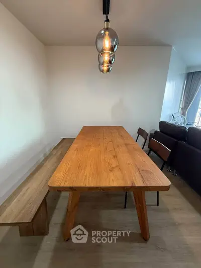 Modern dining area with wooden table and bench, stylish lighting, and cozy living room view.