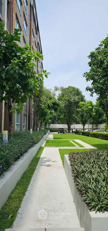 Lush garden pathway beside modern apartment building with vibrant greenery and serene ambiance.