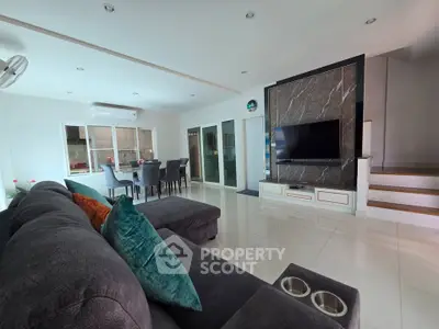 Spacious modern living room with sleek design and dining area, featuring a large TV and comfortable seating.