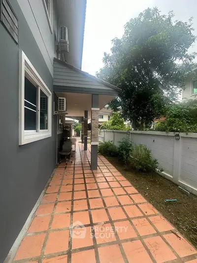 Charming exterior walkway with tiled path and lush greenery, perfect for serene outdoor living.