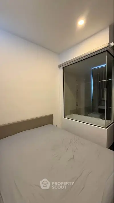 Modern bedroom with unique glass wall feature overlooking bathroom, creating an open and airy ambiance.