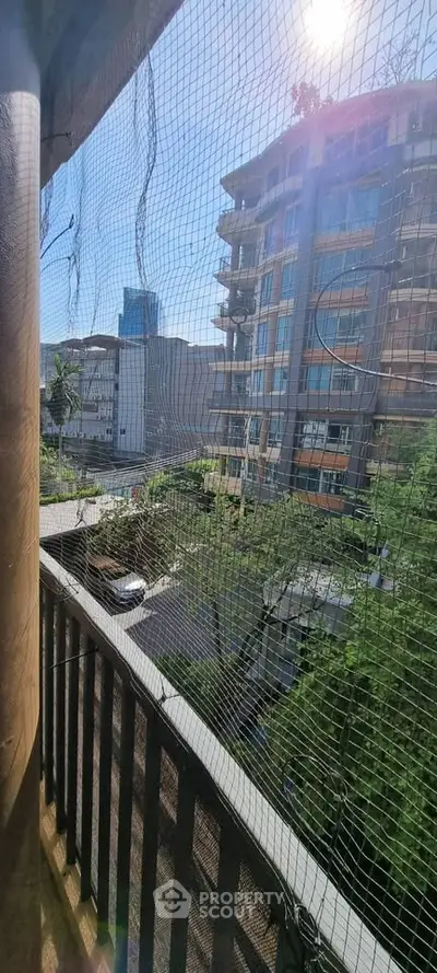 Urban balcony view with safety netting overlooking modern buildings and street below.