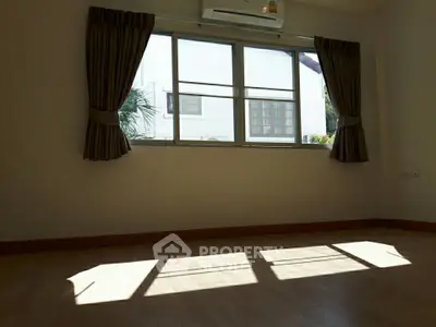 Spacious sunlit room with large window and elegant curtains, perfect for a cozy living space.