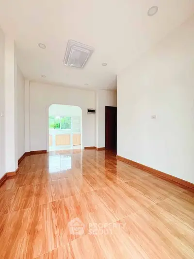 Spacious empty room with wooden flooring and bright natural light, ideal for customization.