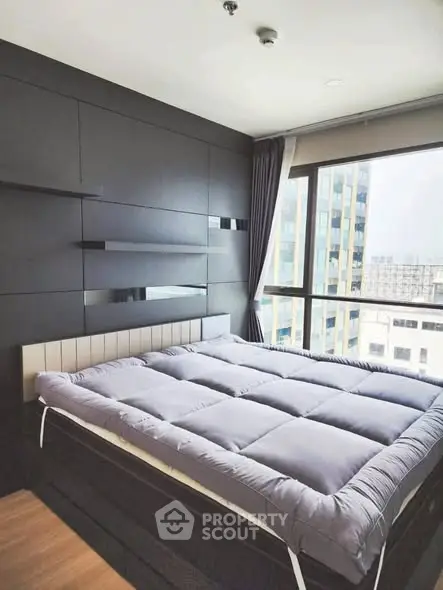 Modern bedroom with large window and city view, featuring sleek black paneling and cozy bedding.
