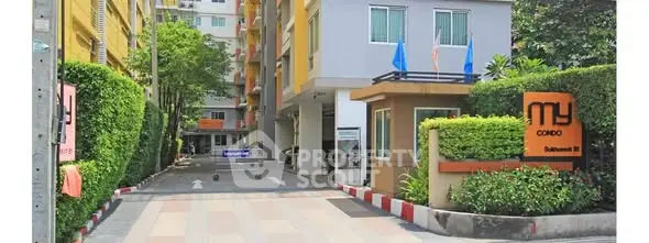 Modern condo entrance with lush greenery and secure access in vibrant urban setting.