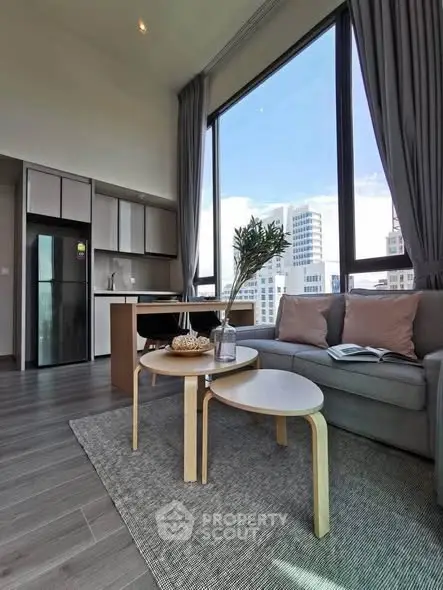 Modern living room with large windows and city view, featuring stylish furniture and open kitchen layout.