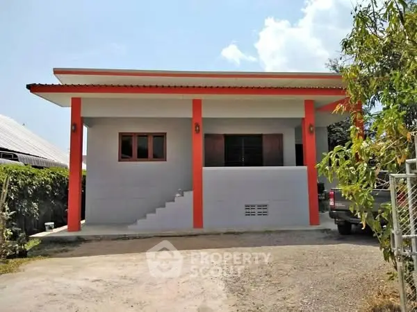 Modern single-story house with vibrant orange accents and a spacious driveway.