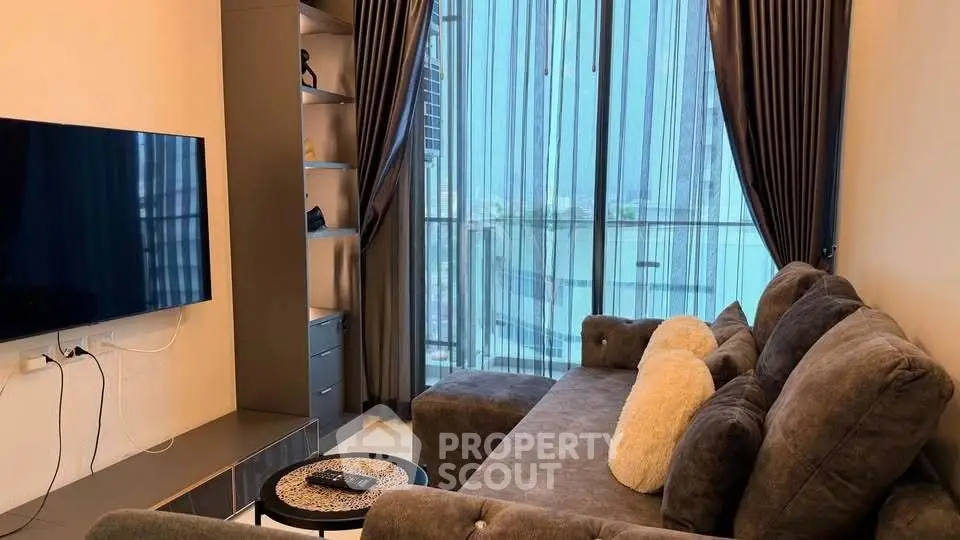 Modern living room with plush sofa and large TV, featuring floor-to-ceiling windows and elegant curtains.