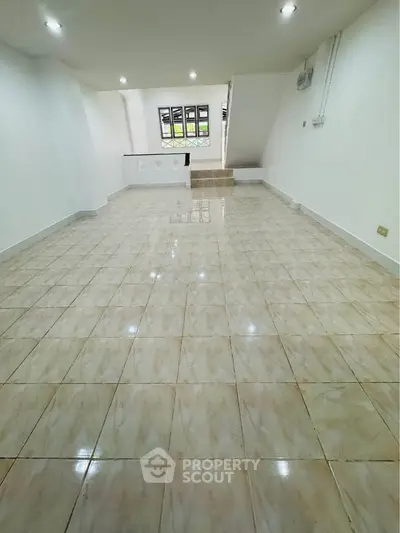 Spacious tiled living area with modern lighting and staircase, perfect for family gatherings.