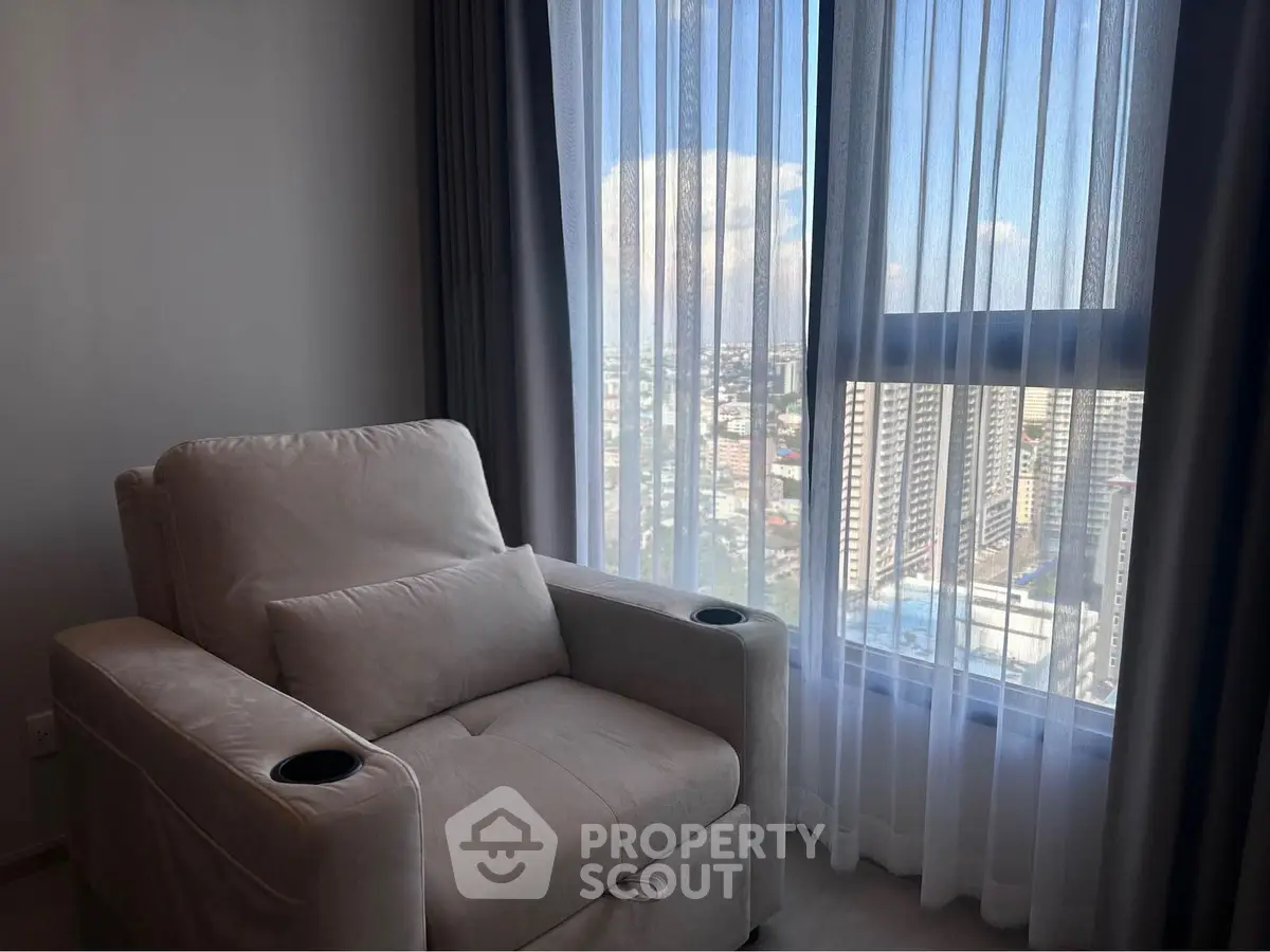 Cozy living room with plush armchair and panoramic city view through large window.