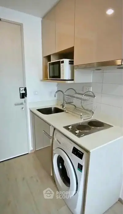 Compact modern kitchen with washing machine and microwave in sleek apartment.