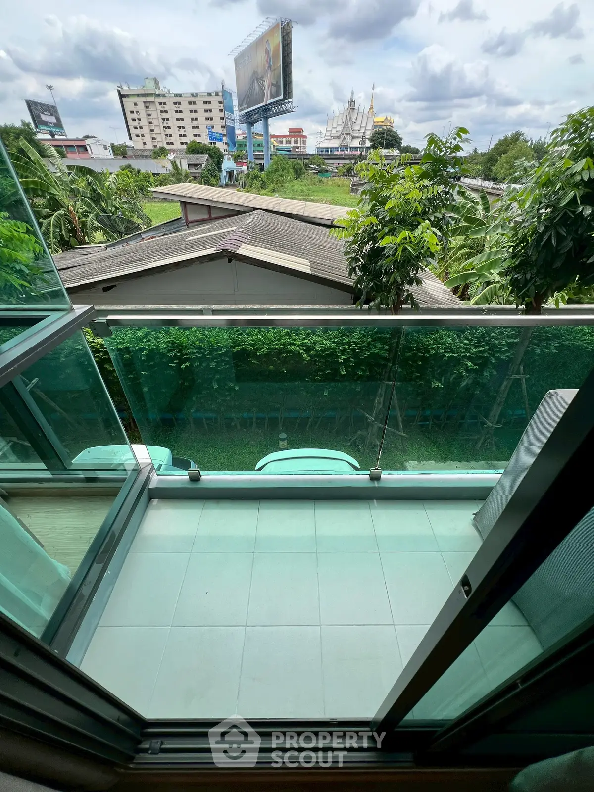 Modern balcony with glass railing offering cityscape view and lush greenery.