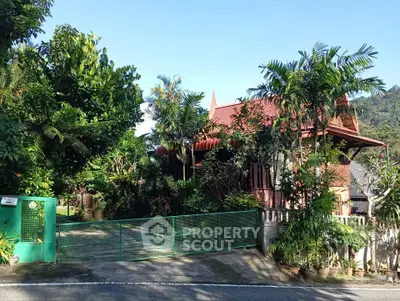 Charming tropical house with lush garden and green gate, perfect for nature lovers.