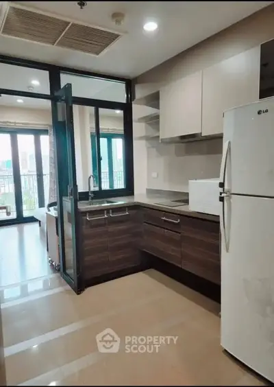Modern kitchen with sleek cabinetry and large fridge, opening to a bright balcony with city views.