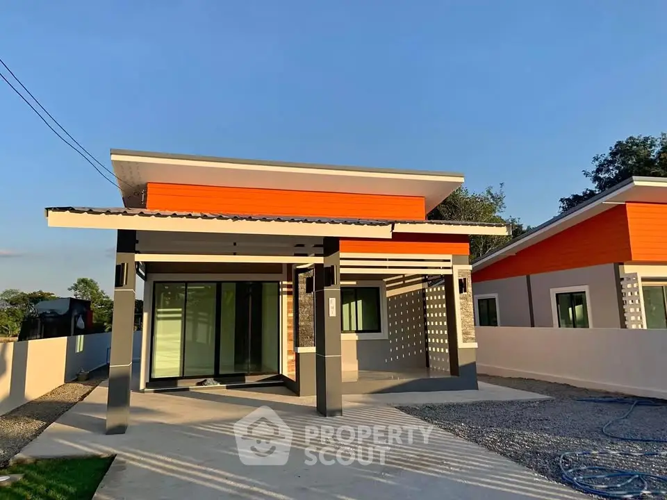 Modern single-story house with vibrant orange accents and spacious driveway.